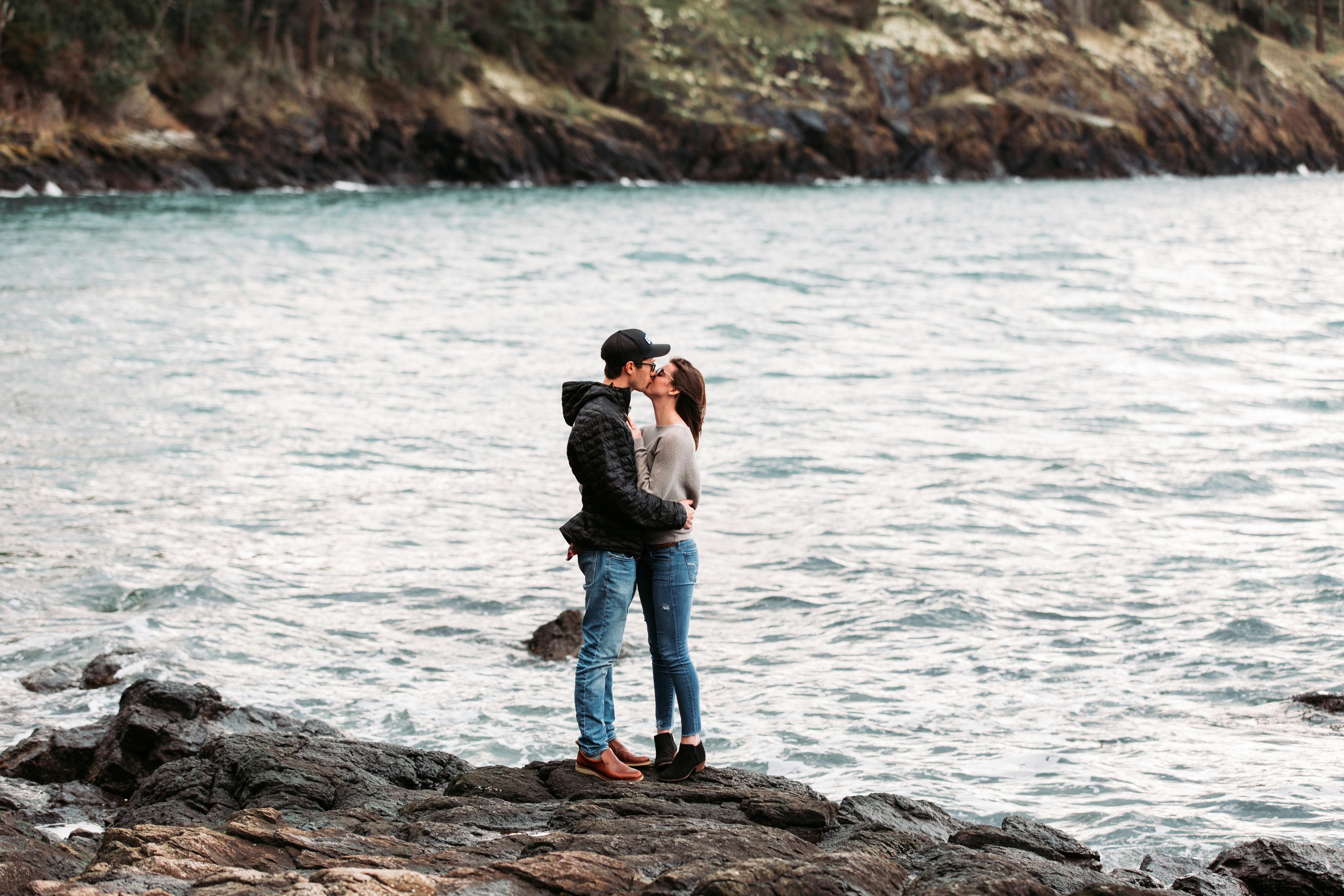 couple kissing on rock beside sea during daytime